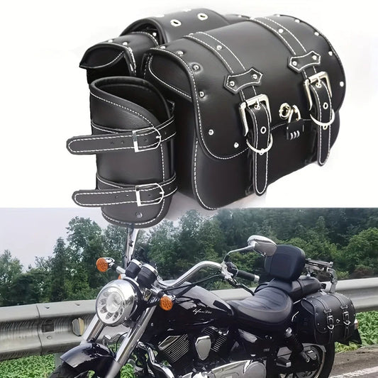 A pair of black leather saddle bags with silver buckles, displayed on a motorcycle in a rural setting.